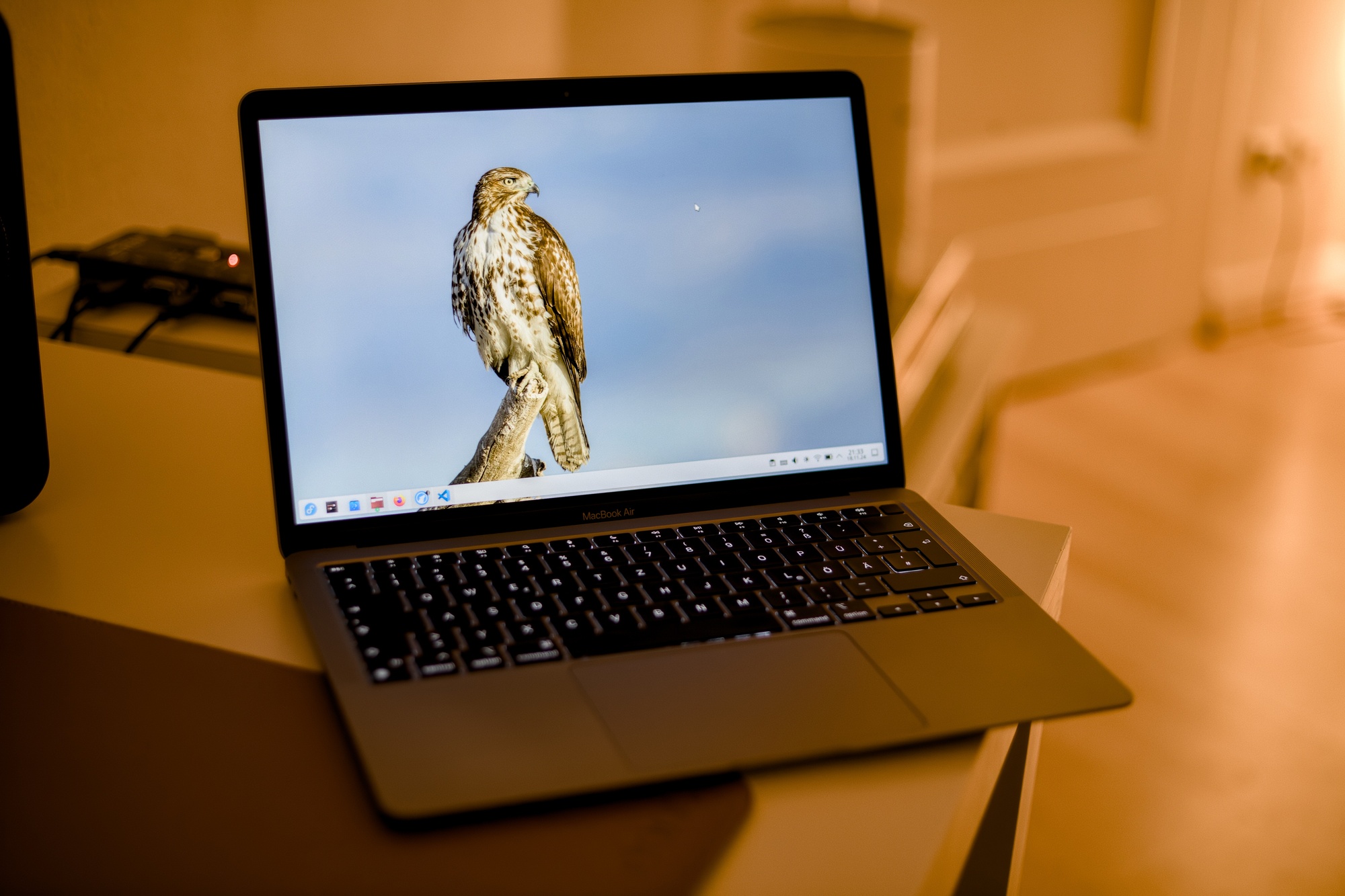 An opened MacBook Air M1 standing on a table. It is showing the desktop of KDE Plasma 6 with the floating task bar at the bottom. The desktop background is a bird of prey.